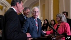 FILE - Senate Minority Leader Mitch McConnell, R-Ky., center, is helped by Sen. John Barrasso, R-Wyo., after freezing in midsentence at the microphone during a news conference, at the Capitol in Washington, July 26, 2023.