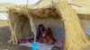 FILE - A displaced woman and her children sit in the shade of a straw hut at a camp in southern Gadaref state, for people who fled Khartoum and Jazira states in war-torn Sudan, March 20, 2024.
