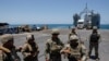 U.S. soldiers stand at Trident Pier, a temporary pier to deliver aid, off the Gaza Strip, amid the ongoing conflict between Israel and Hamas, near the Gaza coast, June 25, 2024, as an aid truck drives off a ship in the background.