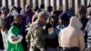FILE - A member of US Customs and Border Protection tries to control a group of migrants as hundreds gather along the border after breaking through gaps in the border wall Dec. 5, 2023, in Lukeville, Ariz. 