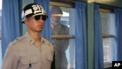FILE - A North Korean soldier looks through a window as a South Korean stands guard at the U.N. truce village building that sits on the border of the Demilitarized Zone (DMZ), in Panmunjon, South Korea. 