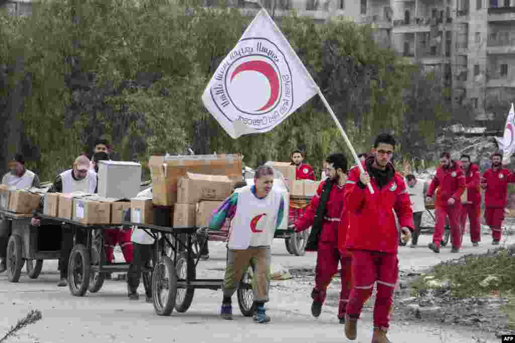 Members of the Syrian Red Crescent group escort Syrians and move aid supplies from a rebel-controlled area to a regime-held area of the northern Syrian city of Aleppo through the Garage al-Hajz crossing in the Bustan al-Qasr district.