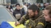 A Ukrainian serviceman writes on a Ukrainian national flag, an apparent keepsake for local residents, as people celebrate after Russia's retreat from Kherson city, in downtown Kherson, Ukraine Nov. 12, 2022.