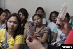 FILE - A community health worker holds up contraceptives during a lecture on family planning at a reproductive health clinic run by an NGO in Tondo city, metro Manila, Jan. 12, 2016.