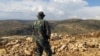 FILE - Hezbollah fighter looks toward Syria while standing in the fields of the Lebanese border village of Brital, Lebanon. 