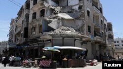 FILE - People walk past a damaged building in the city of Idlib, Syria, May 25, 2019.