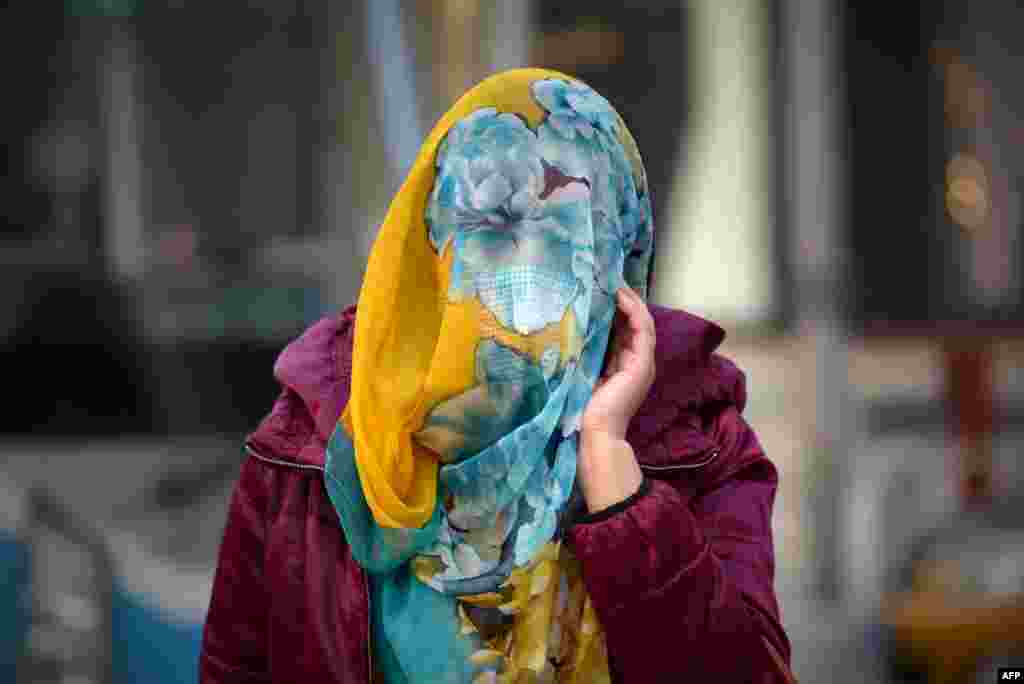 A woman wears a scarf as she walks along a street in Beijing, China.