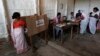 A woman (L) casts her vote with an electronic voting machine as others get their voting slip from an officer at a polling station in Majuli, a large river island in the Brahmaputra river, Jorhat district, in the northeastern Indian state of Assam, April 7