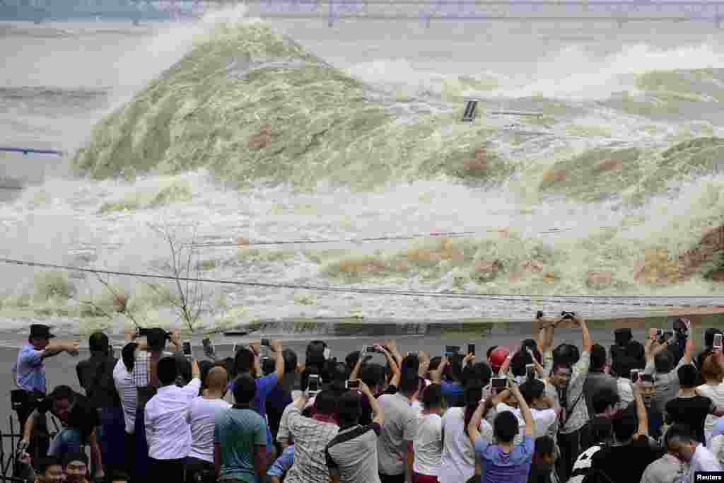 People take pictures as they watch waves caused by a tidal bore on the bank of the Qiantang River, in Hangzhou, Zhejiang province, China, Sept. 30, 2015.