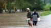 Women wade through flood waters after a seasonal river burst its banks following heavy rainfall in Kitengela municipality of Kajiado County, near Nairobi, Kenya, May 1, 2024. 