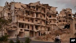 FILE - Motor cycles ride past buildings destroyed during the fighting in the northern town of Ariha, in Idlib province, Syria.