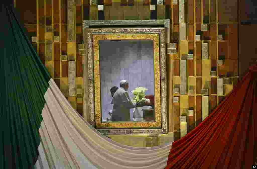 Pope Francis, seen on the other side of the framed glass that usually holds the image of the Virgin of Guadalupe, holds a flower bouquet as he prays to her inside a private room at the Basilica built in her honor, during Mass in Mexico City, Feb. 13, 2016.
