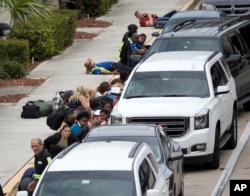 People take cover outside Fort Lauderdale-Hollywood International Airport in Fort Lauderdale, Fla., after a shooter opened fire inside a terminal, Jan. 6, 2017.