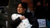 FILE - A mother carries her baby wrapped in a blanket in Beijing.
