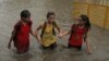 FILE - Indian girls hold hands and wade through a waterlogged street .