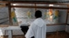 FILE - A priest watches as health workers dressed in Ebola protective suits prepare the body of an Ebola patient for burial at the Ebola treatment center in Butembo, in the Democratic Republic of Congo, March 26, 2019. 