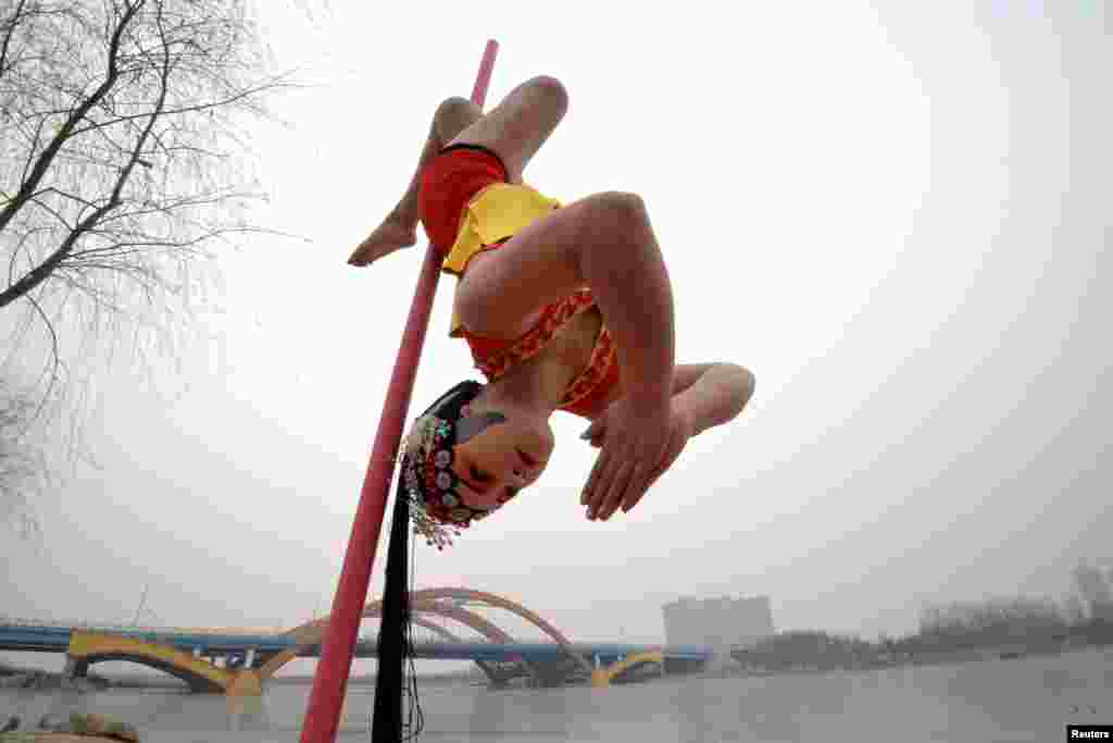 A woman wearing traditional opera make-up performs pole dance by the side of a lake under sub-zero temperatures, in Handan, Hebei province, China, Jan. 20, 2016.