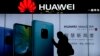 FILE - A woman browses her smartphone as she walks by a Huawei store at a shopping mall in Beijing, Dec. 11, 2018. 