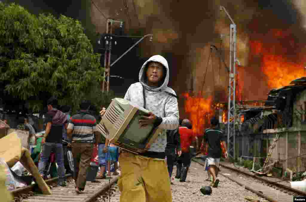 A man carries a television while a fire ranges over a slum area next to railway tracks in Kampung Bandan, North Jakarta, Indonesia.