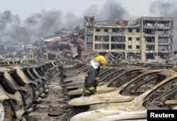 A firefighter walks among damaged vehicles as smoke rises amidst shipping containers at the site of explosions, at Binhai new district in Tianjin, China, Aug. 14, 2015.