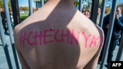 An activist stands naked, wrapped in a rainbow flag, in a mock cage in front of the Chancellery in Berlin on April 30, 2017, during a demonstration calling on Russian President to put an end to the persecution of gay men in Chechnya. / AFP Photo
