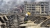 A firefighter walks among damaged vehicles as smoke rises amid shipping containers at the site of explosions, in Tianjin, China, Aug. 14, 2015.