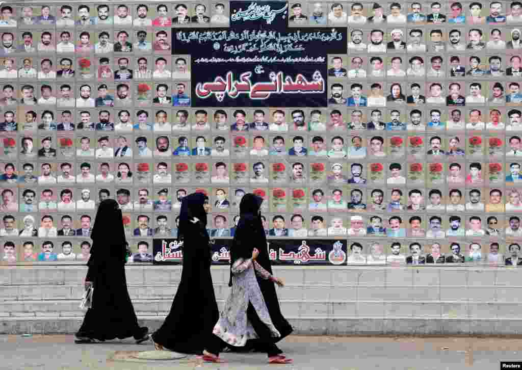 Para perempuan Muslim Syiah melewati tembok peringatan nama-nama korban tewas pemboman bulan Maret tahun 2013, di Karachi, Pakistan.