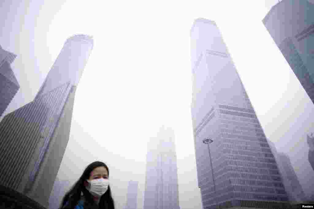 A woman wearing a mask walks below skyscrapers amid heavy smog in the financial district of Pudong, in Shanghai, China. China's first-ever red alert for pollution was in effect earlier this week.