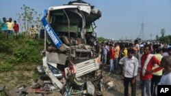 People stand near the wreckage of a bus that collided with a truck in Barabanki district, Uttar Pradesh state, India, Oct.7, 2021.