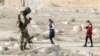 file - A Syrian army soldier looks at his mobile as people visit the ruins of the historic city of Palmyra ahead of a musical event at its amphitheater, Syria, May 6, 2016.