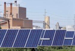 A solar panel array collects sunlight, with the Fremont, Nebraska, May 31, 2018, with a power plant seen behind it.