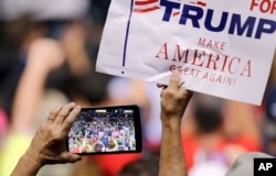 FILE - A supporter holds up a sign and records on his phone as President Donald Trump speaks.