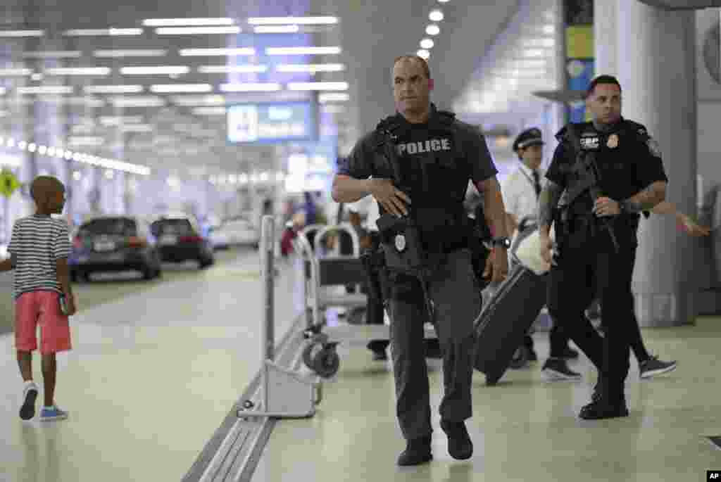 Petugas polisi dari wilayah Miami-Dade, kiri, dan petugas Pabean dan Perlindungan Perbatasan AS, kanan, berpatroli di luar area kedatangan di Bandara Internasional Miami di Miami, Florida. Ada peningkatan tindakan pengamanan di bandara selama libur Hari Kemerdekaan di penghujung pekan ini setalah adanya serangan teroris hari Selasa di Bandara Internasional Ataturk Istanbul, Turki.