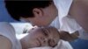 In this undated photo made available by Scott Anger & Bob Sacha for the Open Society Foundations, in Cherkasy, Ukraine, Nadezhda Zhukovsky, 50, kisses her sleeping son Vlad, who died of brain cancer last year at age 27, before going to the local pharmacy 