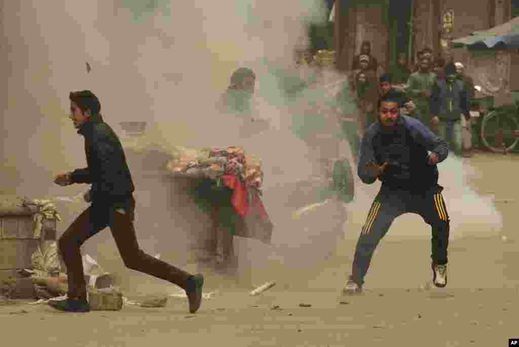 Kashmiri protesters run as a tear gas shell explodes near them during a protest in Srinagar, India, against an intended enforcement of food safety act which will limit the subsidized ration per person in the state to 5 kilos from the present 30 kilos.