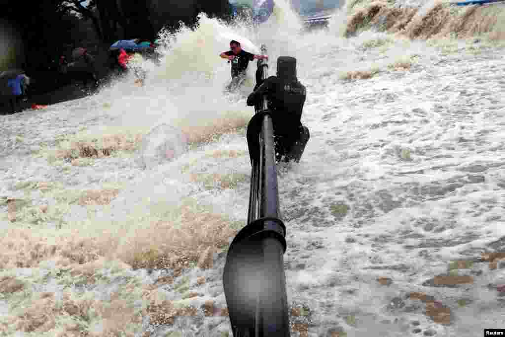 A paramilitary policeman holds onto a fence as tourists dodge tidal waves increased under the influence of Typhoon Dujuan, at the bank of Qiantang river, in Hangzhou, Zhejiang province, China. China ordered tens of thousands of boats back to shore and closed tourist attractions as a typhoon made landfall in the eastern province of Fujian after leaving two dead and hundreds injured in Taiwan.