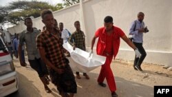 Quelques personnes portent le corps d'une victime de l'explosion de voiture près de l'hôtel Doorbin à Mogadiscio, le 24 février 2018. AFP PHOTO / Mohamed ABDIWAHAB