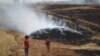 FILE - A man gestures as smoke rises from a burning farmland targeted by what activists said were airstrikes by forces loyal to Syria's President Bashar al-Assad in Maarshmarin village in Idlib countryside, May 24, 2015. 