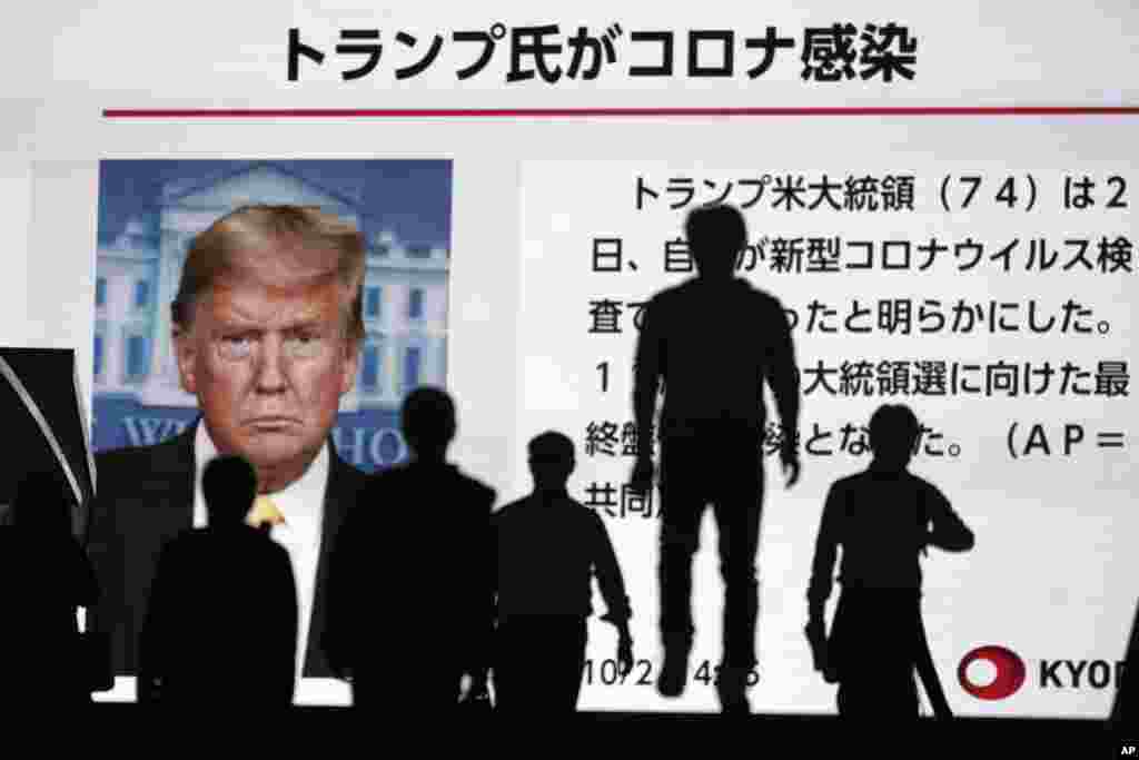 People walk past a screen showing the news report that President Donald Trump has tested positive for the coronavirus, in Tokyo. 