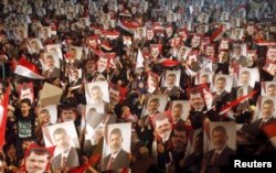 FILE - Members of the Muslim Brotherhood and supporters of Egypt's President Mohamed Mursi hold pictures of him as they react after the Egyptian army's statement was read out on state TV, at the Raba El-Adwyia mosque square in Cairo, July 3, 2013.