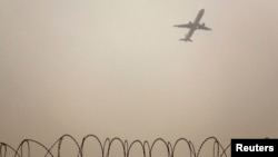 FILE - A plane flies in the polluted air above the airport fences in Beijing, Feb. 22, 2012.