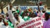 FILE - Demonstrators hold placards as they chant slogans and wave Zimbabwe's national flags during a rally to denounce U.S. and EU economic sanctions, at the National Stadium, in the capital Harare, Oct. 25, 2019. 