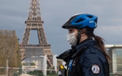 A policewoman wears a mask to protect herself against the spread of the new coronavirus, left, patrols at the garden of the Eiffel Tower in Paris, April 6, 2020.
