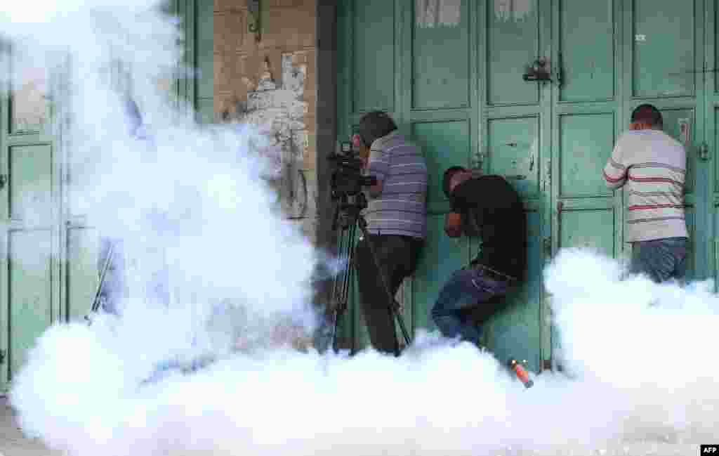 Palestinians take cover from tear gas and protect their ears from a sound grenade fired by Israeli security forces, during a demonstration in the West Bank town of Hebron in solidarity with fellow demonstrators clashing with Israeli police at Jerusalem's flashpoint Al-Aqsa mosque compound.