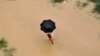 A man uses an umbrella to protect himself from rain as he walks through the flooded banks of river Ganga in the northern Indian city of Allahabad, Aug. 4, 2014. 