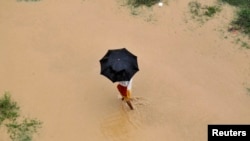 A man uses an umbrella to protect himself from rain as he walks through the flooded banks of river Ganga in the northern Indian city of Allahabad, Aug. 4, 2014. 