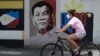 FILE - A woman wearing a protective mask rides her bicycle past an image of Philippine President Rodrigo Duterte in Manila, Philippines, on March 20, 2020. 