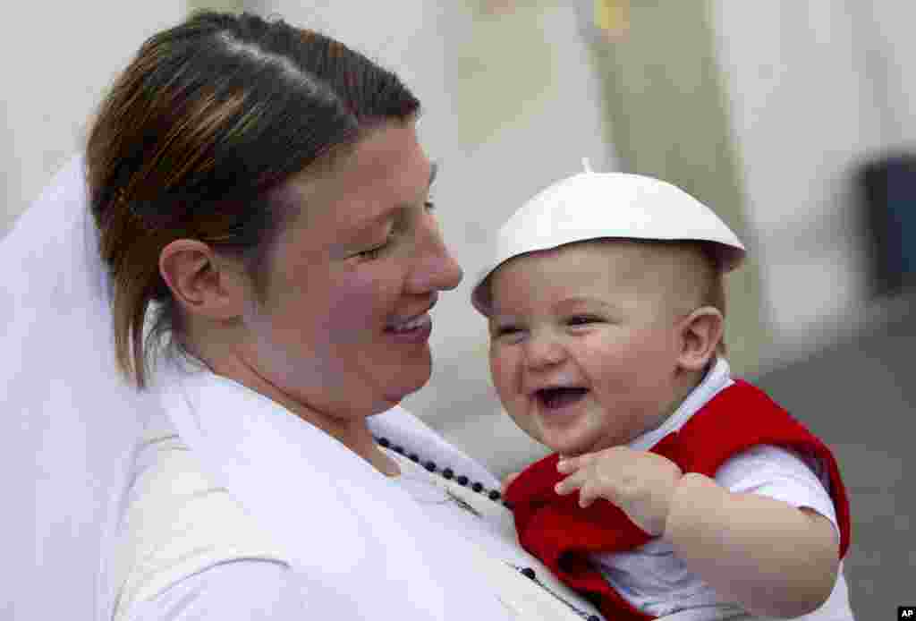 A woman holds a baby wearing a white skull cap, at the end of Pope Francis' weekly general audience, in St. Peter's Square, at the Vatican.