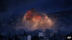 FILE - In this Oct. 20, 2014 file photo, thick smoke and flames erupt from an airstrike by the U.S.-led coalition in Kobani, Syria, as seen from a hilltop on the outskirts of Suruc, at the Turkey-Syria border. For Syrians marking seven years of war…