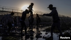 AS tampak di latar belakang saat Joiner, migran Venezuela, menyerahkan putrinya Ivanna di Rio Grande saat mencari masuk ke AS dari perbatasan Ciudad Juarez-El Paso, 20 April 2024. REUTERS/Adrees Latif